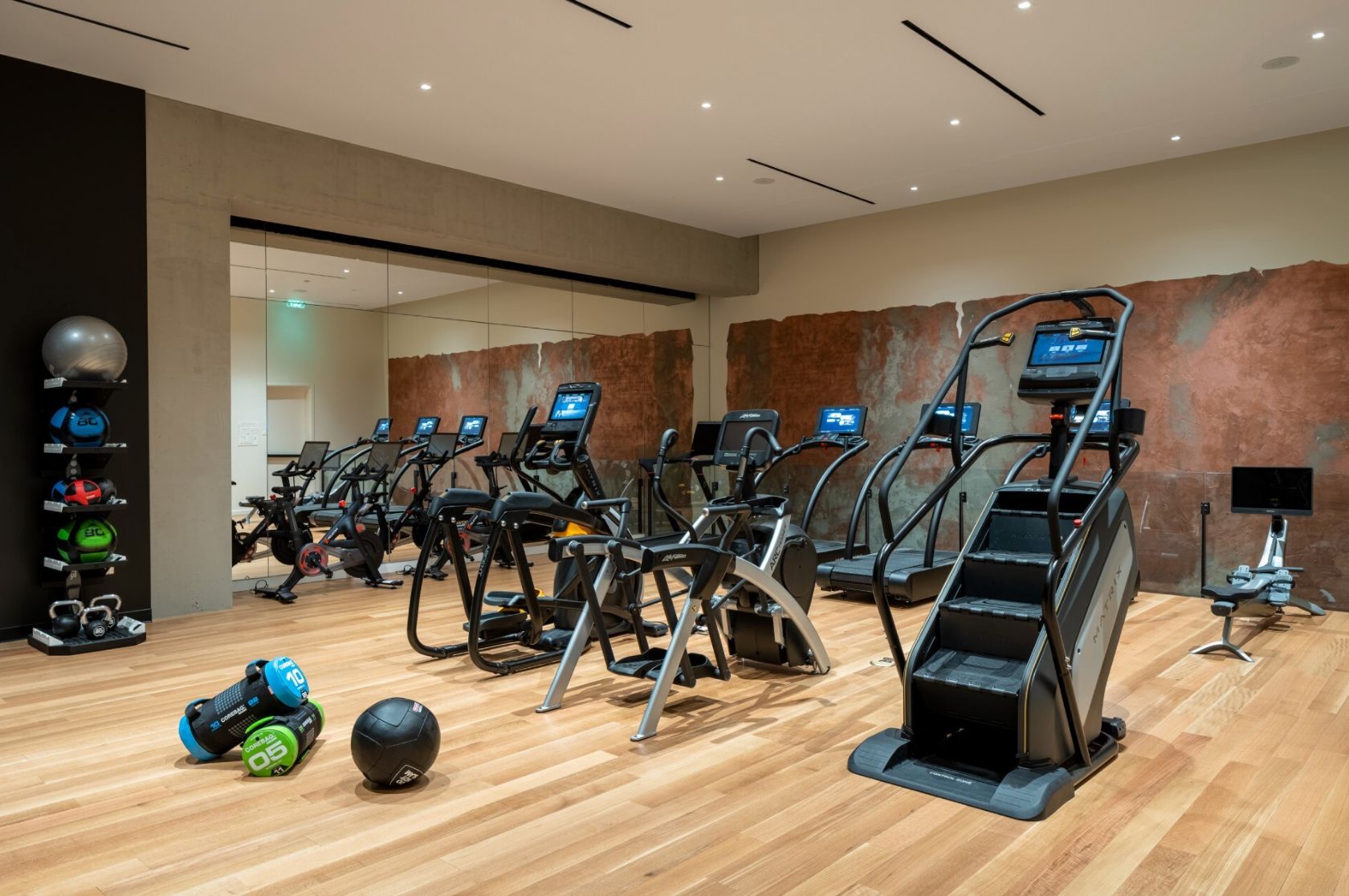 Un gimnasio moderno con varias cintas de correr, equipo de levantamiento de pesas y suelo de madera.