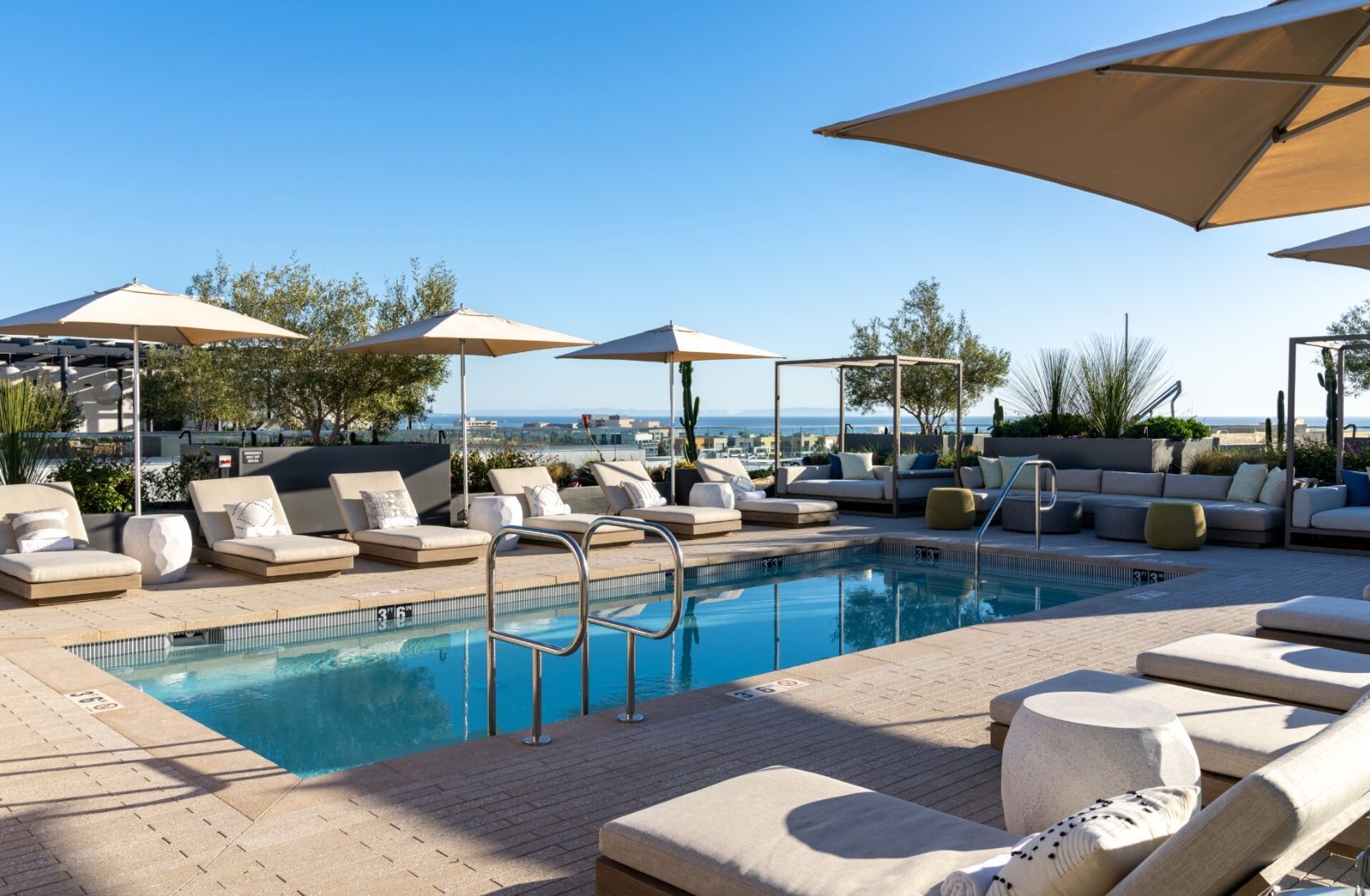 A poolside area with lounge chairs, umbrellas, and a view of the sea.