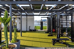 Een buitengymzaal met fitnessapparatuur, een bokszak en potplanten.