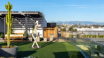 A rooftop terrace with artificial grass, a cactus, a wooden bench, and a sculpture.