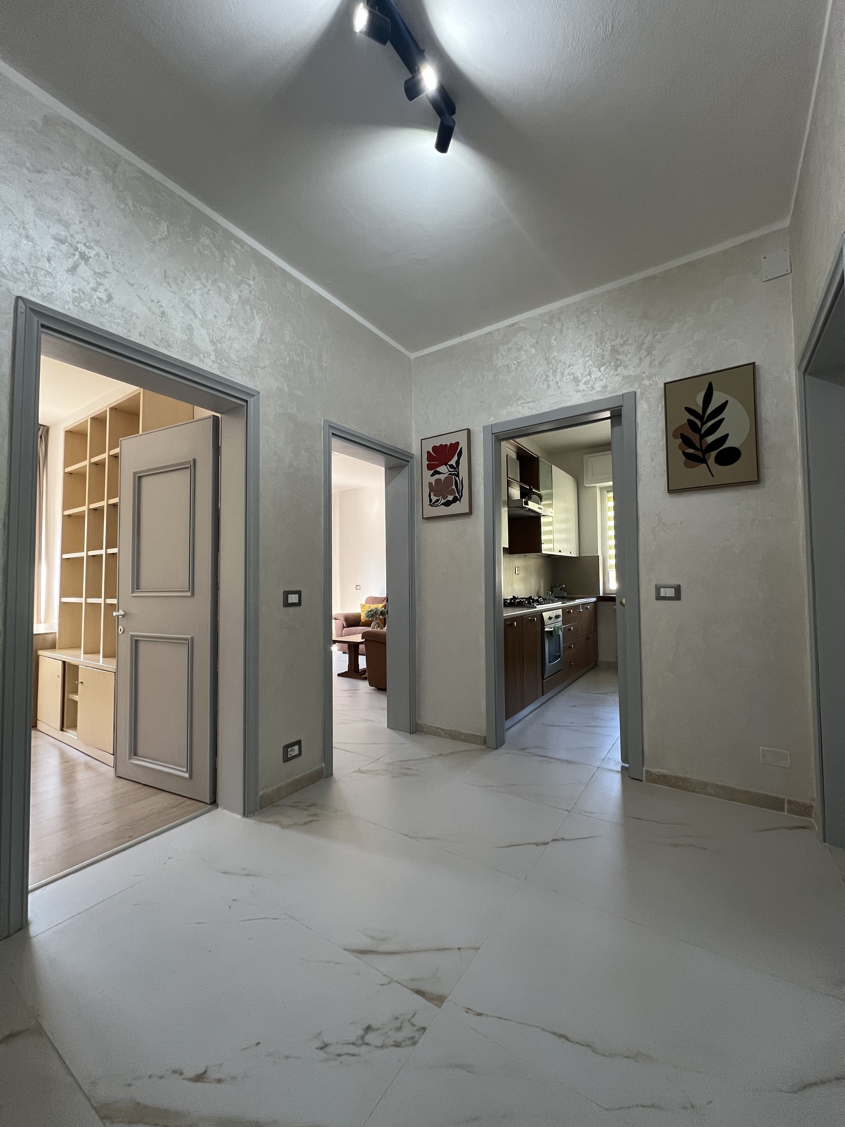 Un hall d’entrée spacieux, avec un coin cuisine visible à travers une porte ouverte, un luminaire au plafond et une œuvre d’art encadrée accrochée au mur.