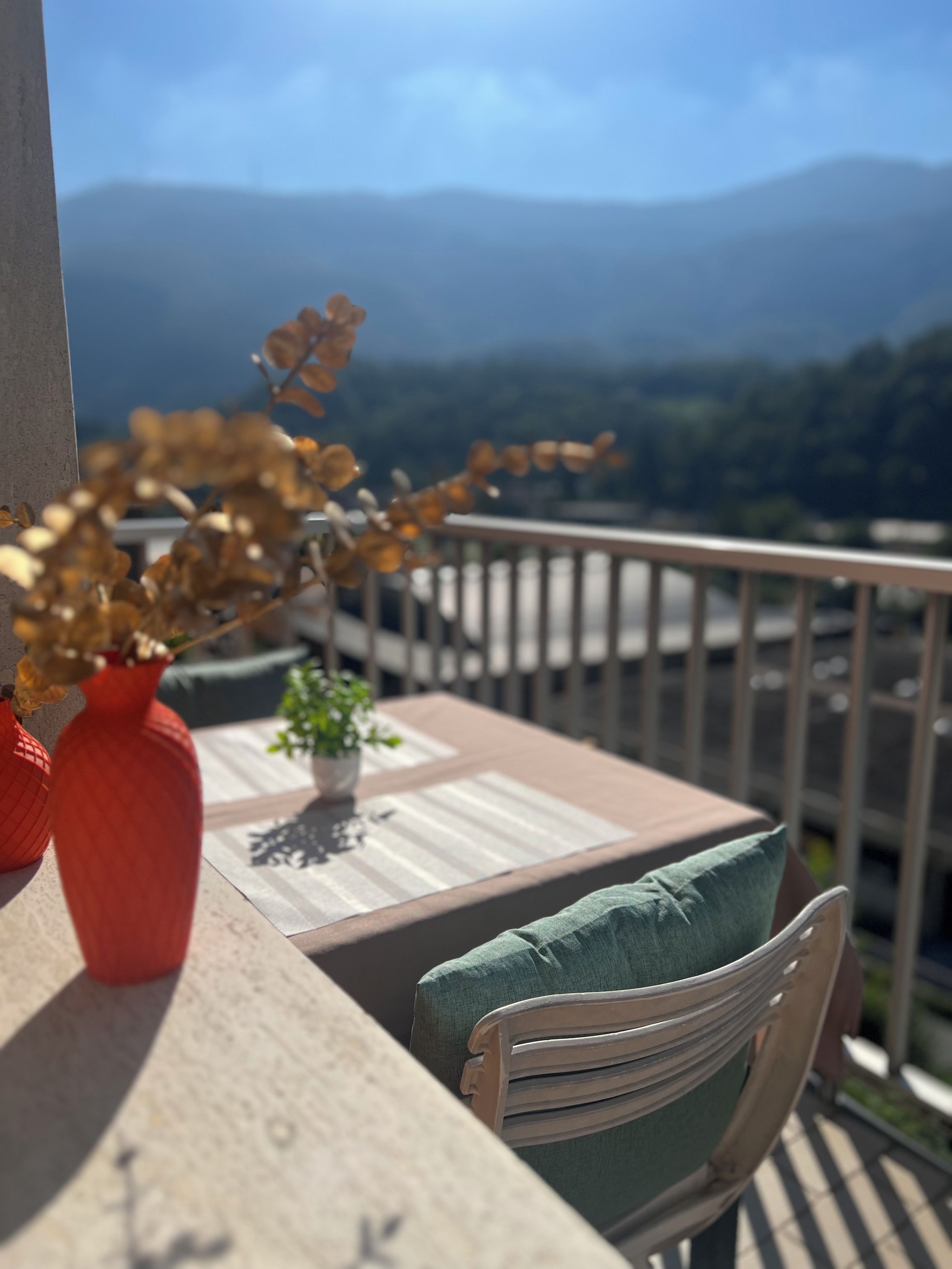 A balcony with a table, chairs, and a vase with dried flowers.