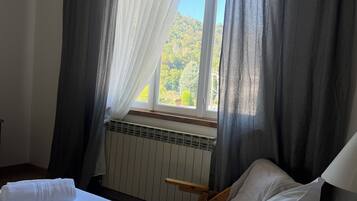 A bedroom with a bed, a window with curtains, a radiator, and a wooden chair.