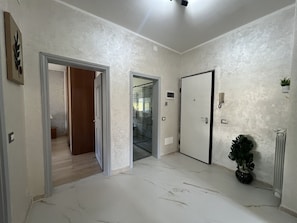 Un pasillo con suelo de mármol, una puerta, un radiador y una planta en maceta.