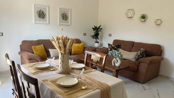 Un coin repas avec une table dressée pour deux personnes, un canapé marron et des œuvres d’art décoratives accrochées au mur.