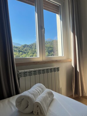 Una cama con una toalla blanca enrollada, una ventana con cortinas y un radiador.