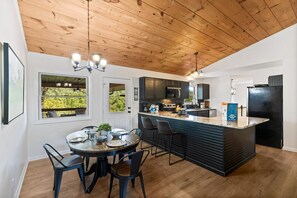 A modern kitchen with a wooden ceiling, a central island with bar stools, and a dining area with a round table and chairs. - Stone Ridge Summit: Pet Friendly, Mtn Views, Hot Tub, Game Room, Firepit + More (Sevierville)