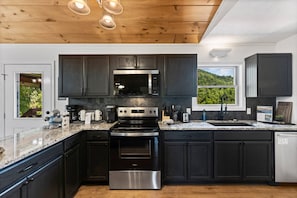 A modern kitchen with dark cabinets, stainless steel appliances, and a granite countertop. - Stone Ridge Summit: Pet Friendly, Mtn Views, Hot Tub, Game Room, Firepit + More (Sevierville)