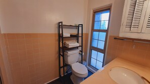 Een kleine badkamer met toilet, een plank met handdoeken, een raam en een wastafel.