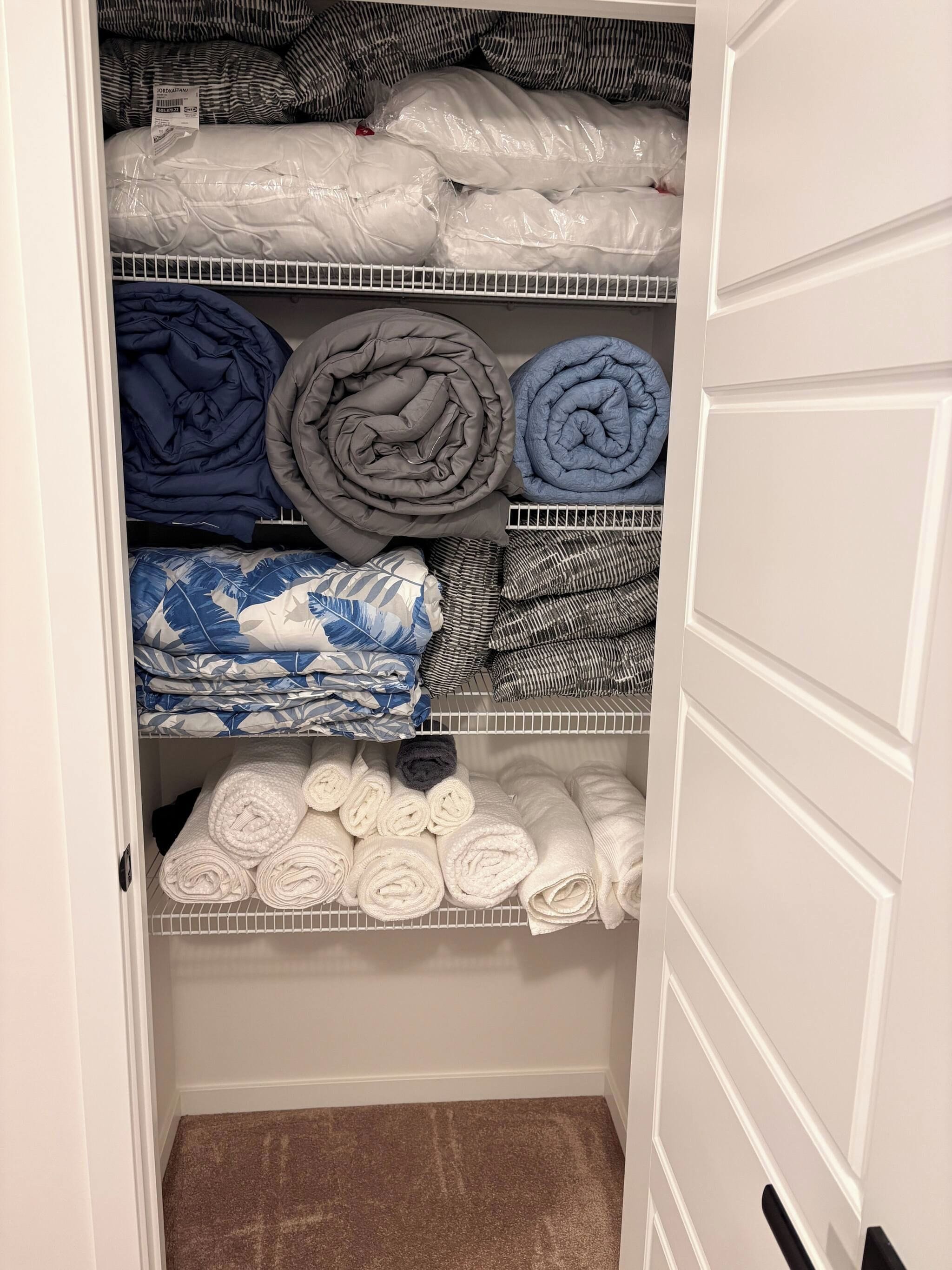 A closet with shelves containing folded bedding and towels.