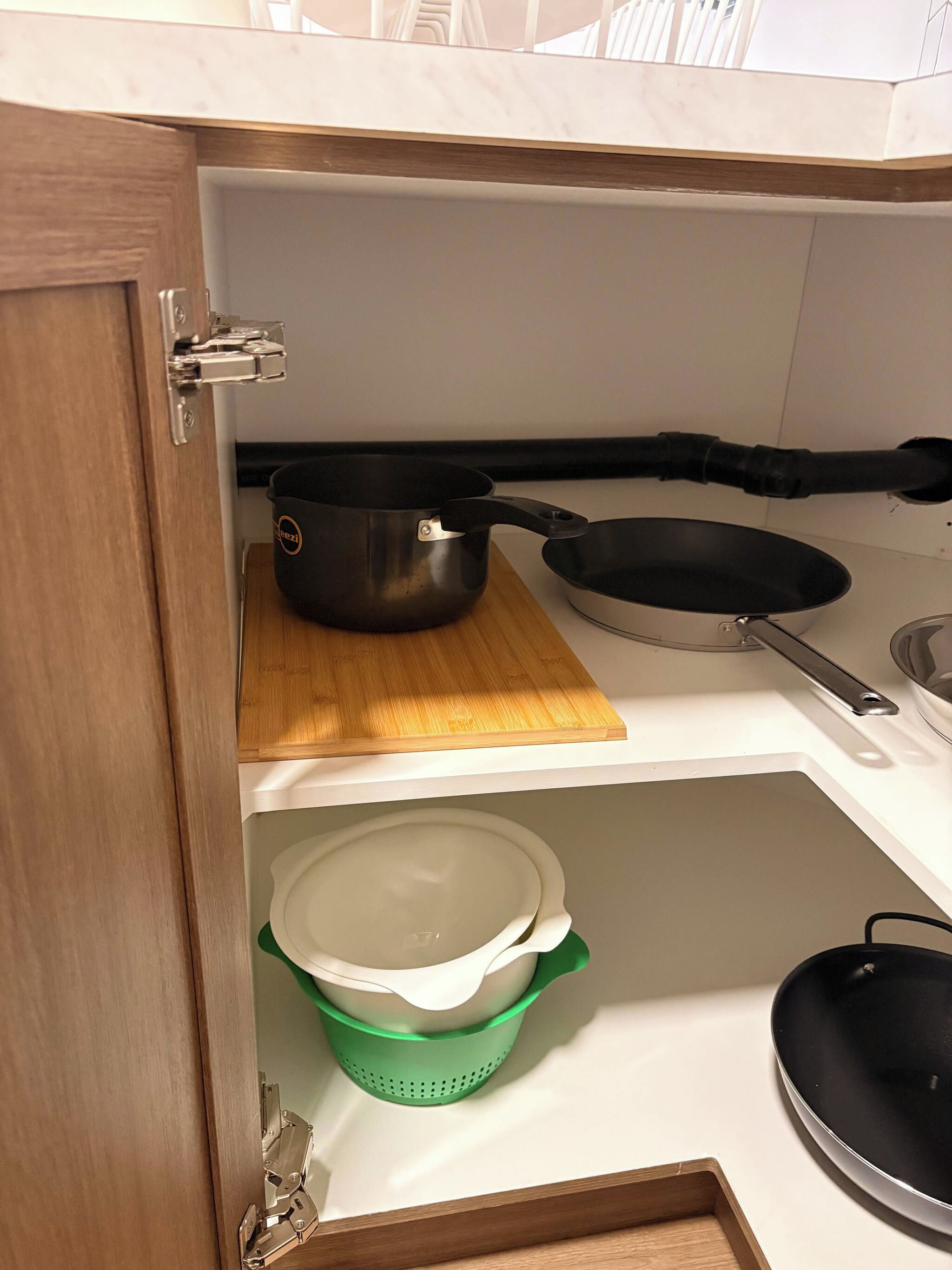 A kitchen with a wooden cutting board, a frying pan, a pot, and a colander.
