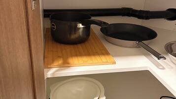 A kitchen with a wooden cutting board, a frying pan, a pot, and a colander.