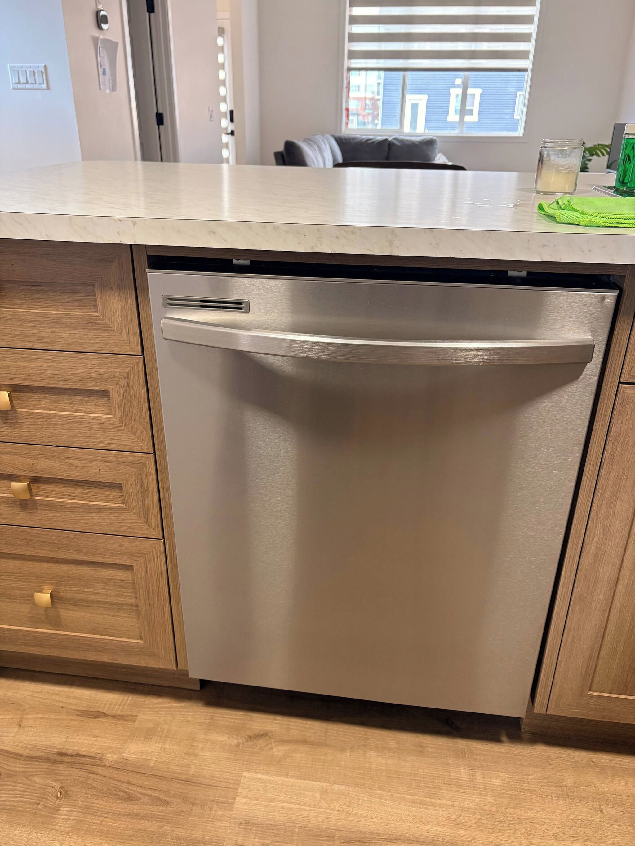 A kitchen with a dishwasher, wooden cabinets, and a window with blinds.