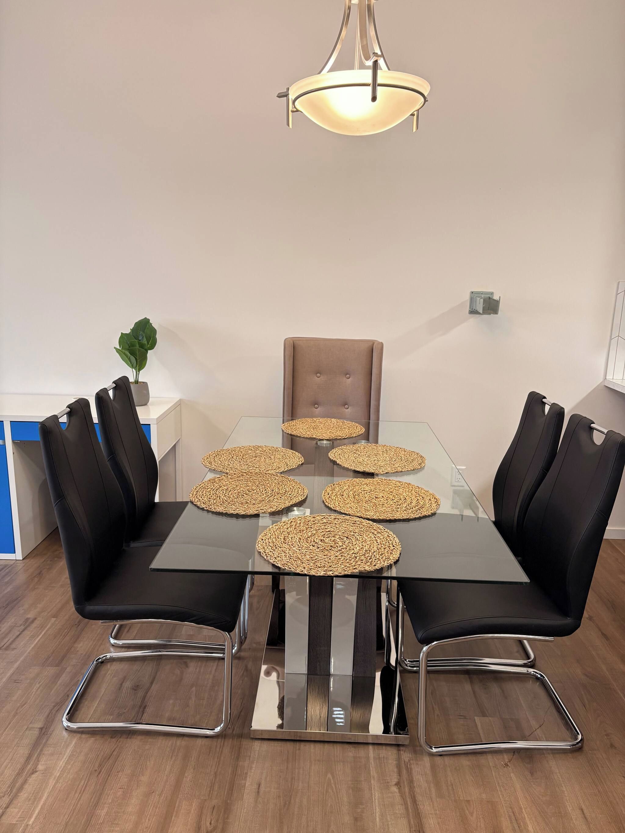 A modern dining area with a glass table, black upholstered chairs, and woven placemats.