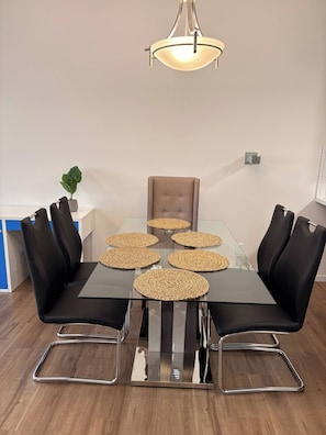 A modern dining area with a glass table, black upholstered chairs, and woven placemats. - Spaciouscalgaryhome l 4 Bedrooms l Sleeps 8 Plus (Calgary)