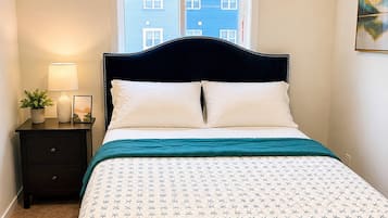 A bedroom with a bed, a nightstand, a lamp, a window, and a view of buildings.