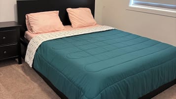 A bedroom with a bed, two pillows, a bedside table, and a window with blinds.
