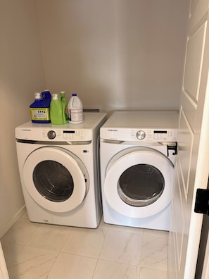 A laundry room with two white Samsung washing machines and a shelf with cleaning supplies. - Spaciouscalgaryhome l 4 Bedrooms l Sleeps 8 Plus (Calgary)