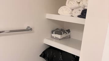 A storage closet with shelves containing folded towels and a black trash bag.
