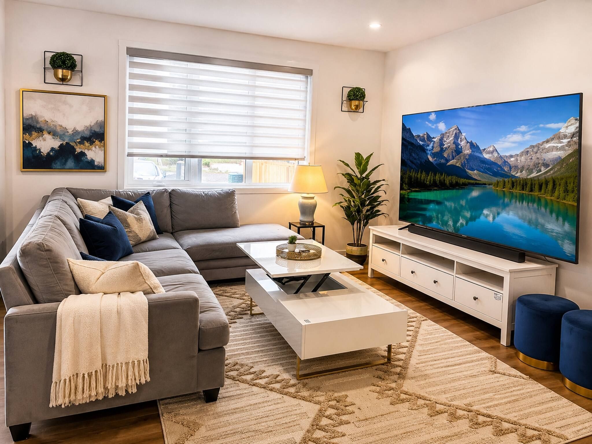 A modern living room with a grey sofa, a coffee table, a TV, and a large window with blinds.