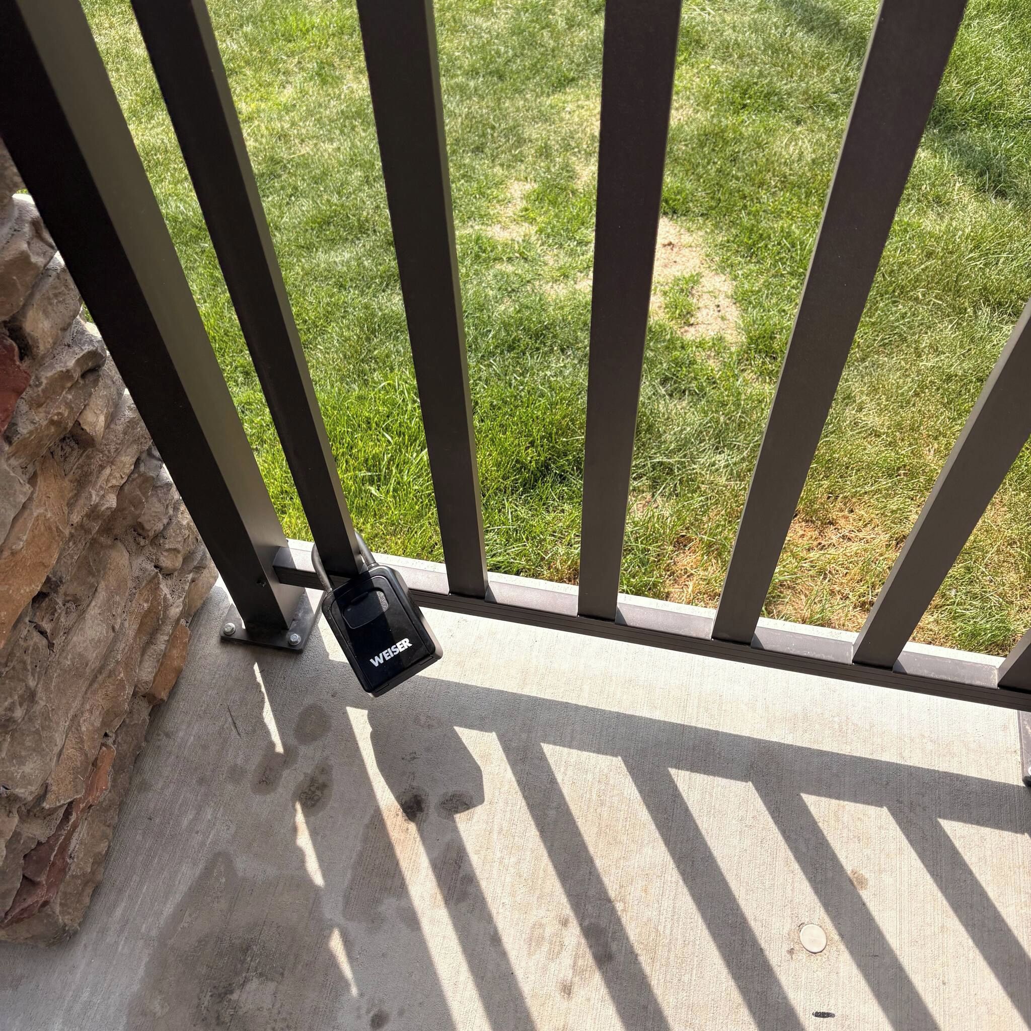 A security lock attached to a metal gate, with a concrete floor and a grassy area in the background.