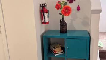 A teal console table with a vase of flowers, a fire extinguisher, and a small shelf with books.