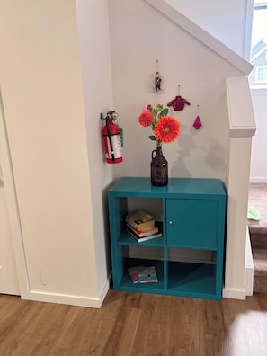 A teal console table with a vase of flowers, a fire extinguisher, and a small shelf with books. - Spaciouscalgaryhome l 4 Bedrooms l Sleeps 8 Plus (Calgary)
