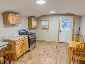 A kitchen with wooden cabinets, a stove, and a dining area with a table and chairs. - Aries | Black Lake Glamping Dome (Hammond)