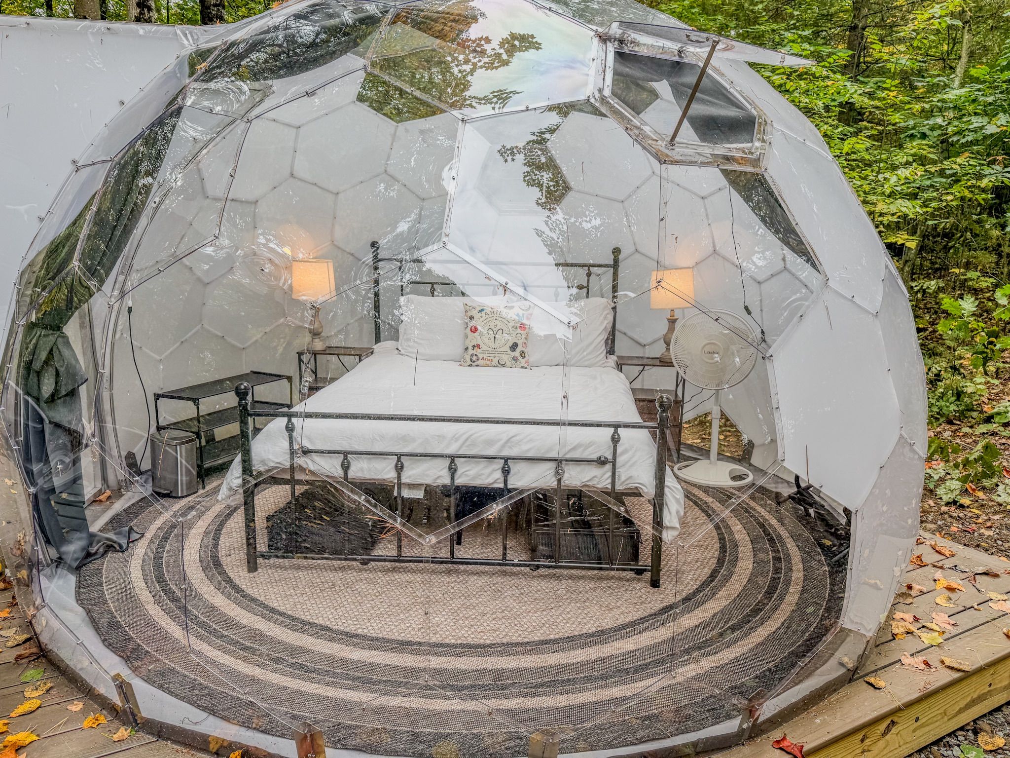 A transparent dome structure with a bed and two lamps, surrounded by a circular patterned floor.