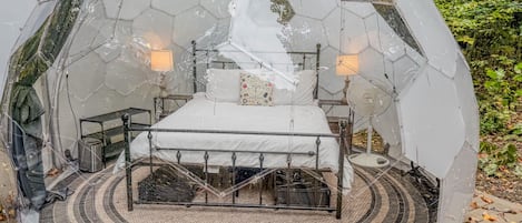 A transparent dome structure with a bed and two lamps, surrounded by a circular patterned floor.