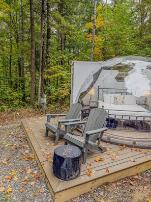 A campsite with a tent, two Adirondack chairs, a small table, and a black stool. - Aries | Black Lake Glamping Dome (Hammond)