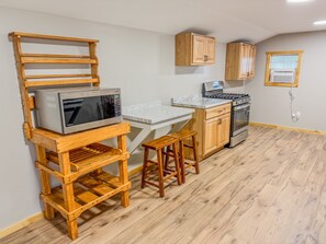 A compact kitchen with wooden cabinetry, a built-in microwave, a stove, and a small wooden table with stools. - Aries | Black Lake Glamping Dome (Hammond)