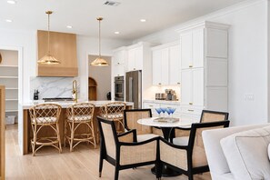 Une cuisine moderne avec des meubles blancs, un îlot central doté de tabourets et des luminaires suspendus.