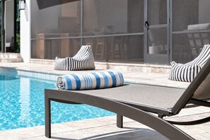 A poolside area with a lounge chair, a towel, and a chair with striped cushions. - Oak and Palm Cottage – New Listing! Family Retreat Private Pool & Spa | Walk to Village, Parks & Beach (Saint Simons Island)