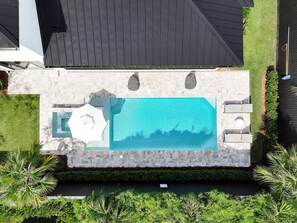 Een zwembad met een terras van steen, omringd door groen en een huis op de achtergrond.