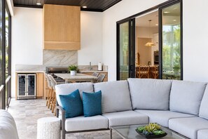 A modern living area with a grey sectional sofa, a glass coffee table, and a view of the kitchen and dining area. - Oak and Palm Cottage – New Listing! Family Retreat Private Pool & Spa | Walk to Village, Parks & Beach (Saint Simons Island)