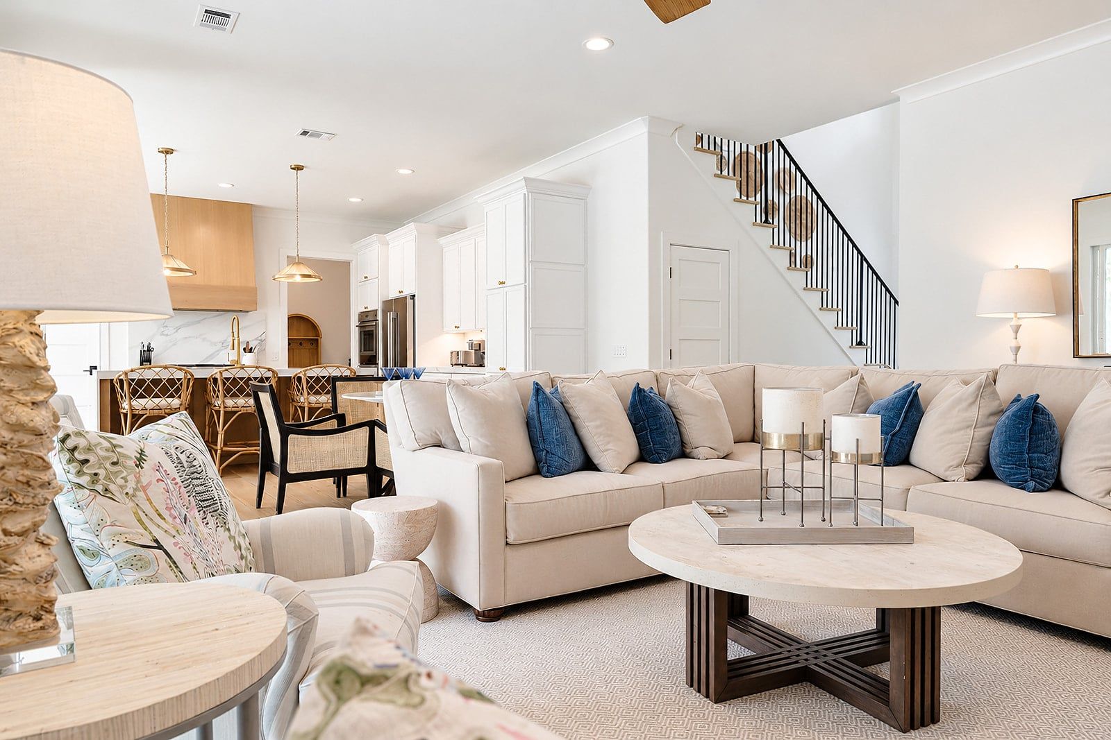 A modern living room with a beige sofa, round coffee table, and a staircase with a black railing.
