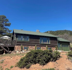Une cabane en rondins avec des fondations en pierre, une porte verte et un balcon agrémenté d’un parasol de patio.