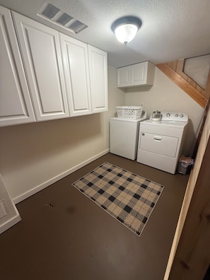 A laundry room with white cabinets, a washing machine, a dryer, and a patterned rug. - Cozy Log Cabin at Blue Skies Ranch, minutes to Palmer Lake (Larkspur)