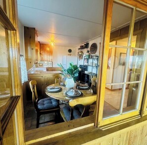 A dining area with a wooden table set for four, surrounded by chairs. A potted plant is on the table, and there is a window with a view of the interior. - Cozy Log Cabin at Blue Skies Ranch, minutes to Palmer Lake (Larkspur)