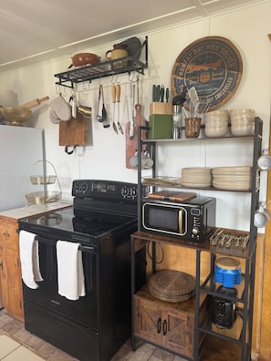 A kitchen with a black stove, a microwave, and various utensils hanging on the wall. - Cozy Log Cabin at Blue Skies Ranch, minutes to Palmer Lake (Larkspur)