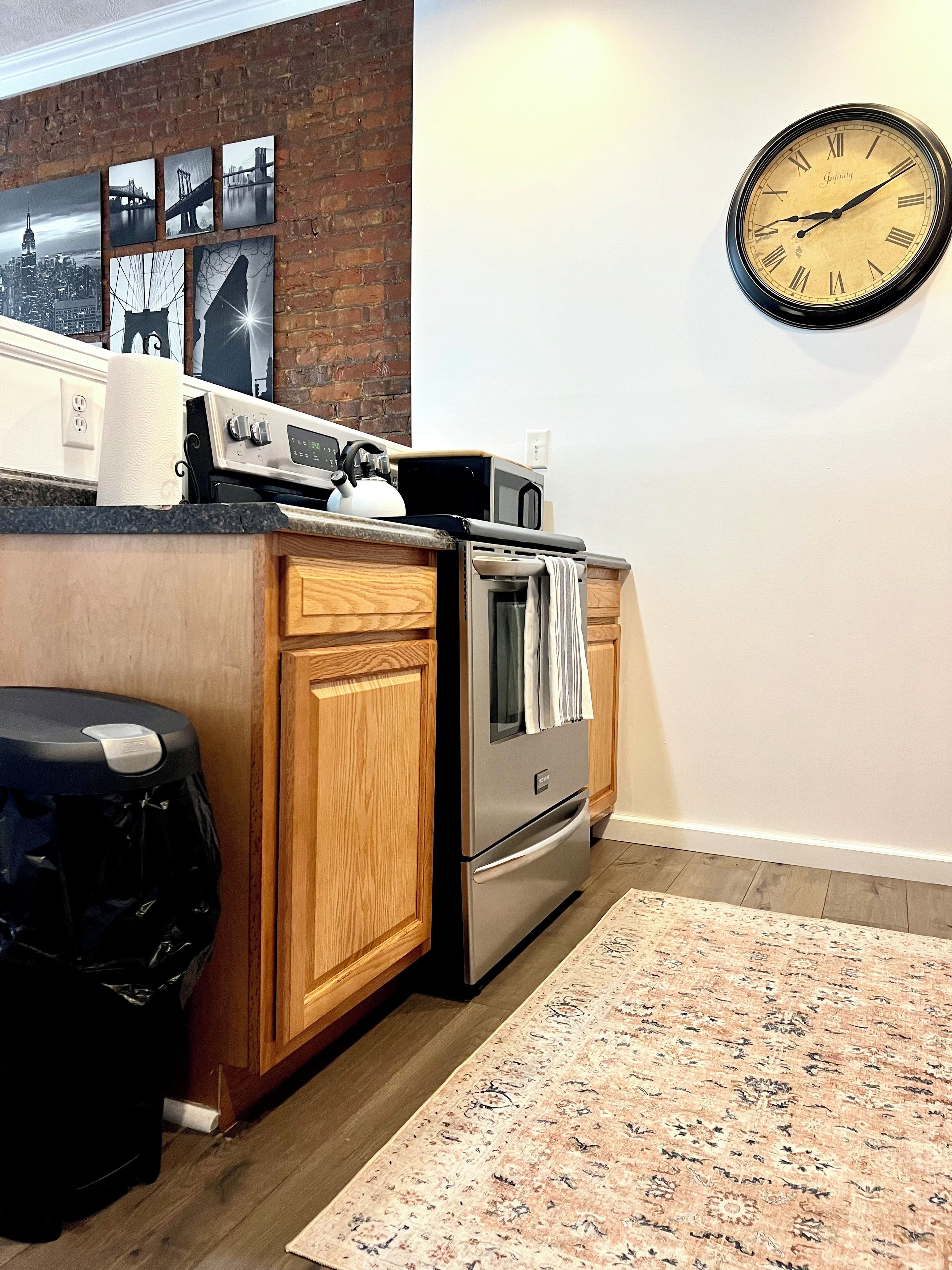 A kitchen with a brick wall, a clock, and a stainless steel refrigerator.