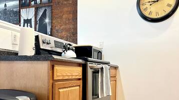 A kitchen with a brick wall, a clock, and a stainless steel refrigerator.
