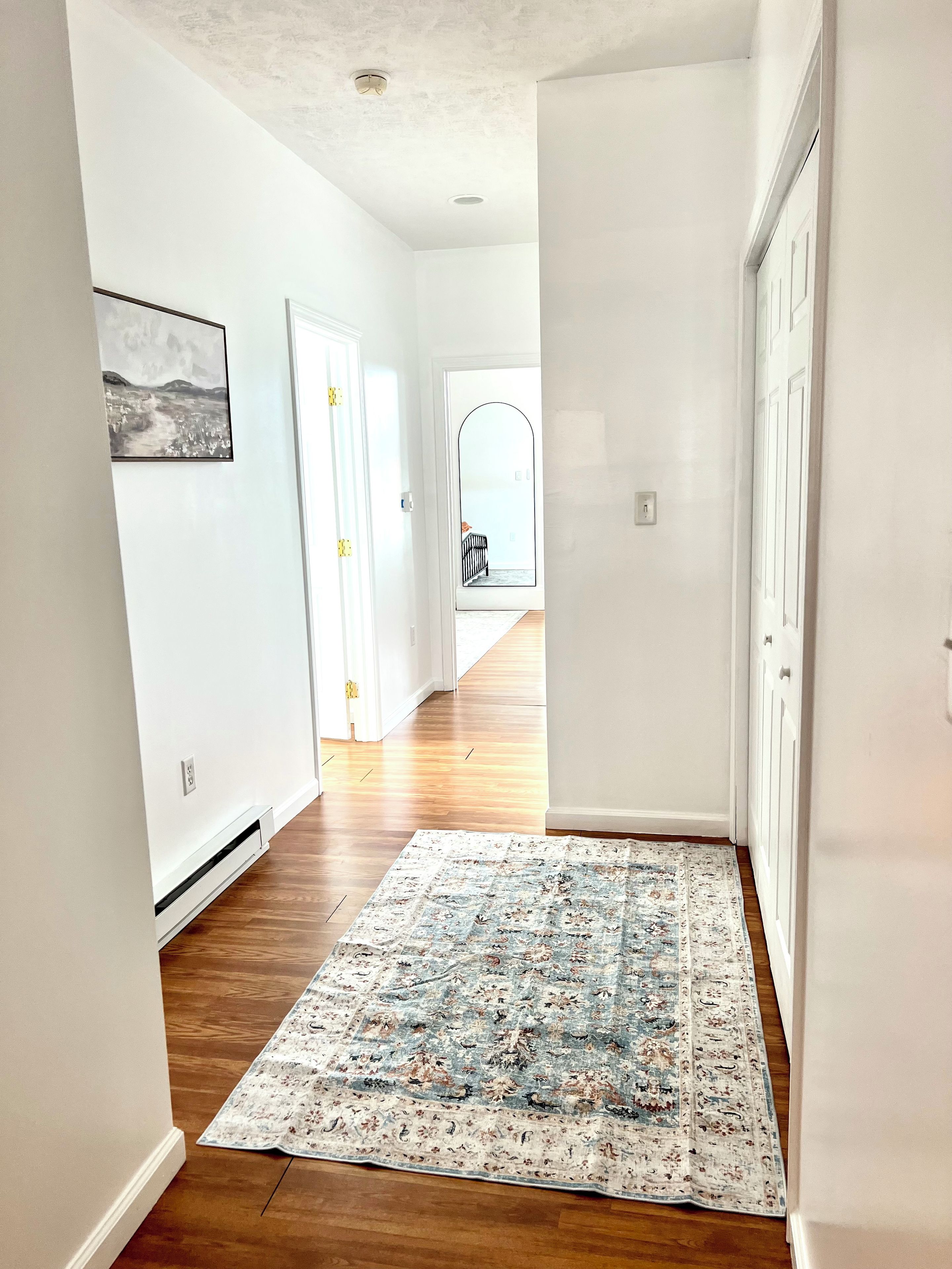 A hallway with a patterned rug, white walls, and wooden flooring.