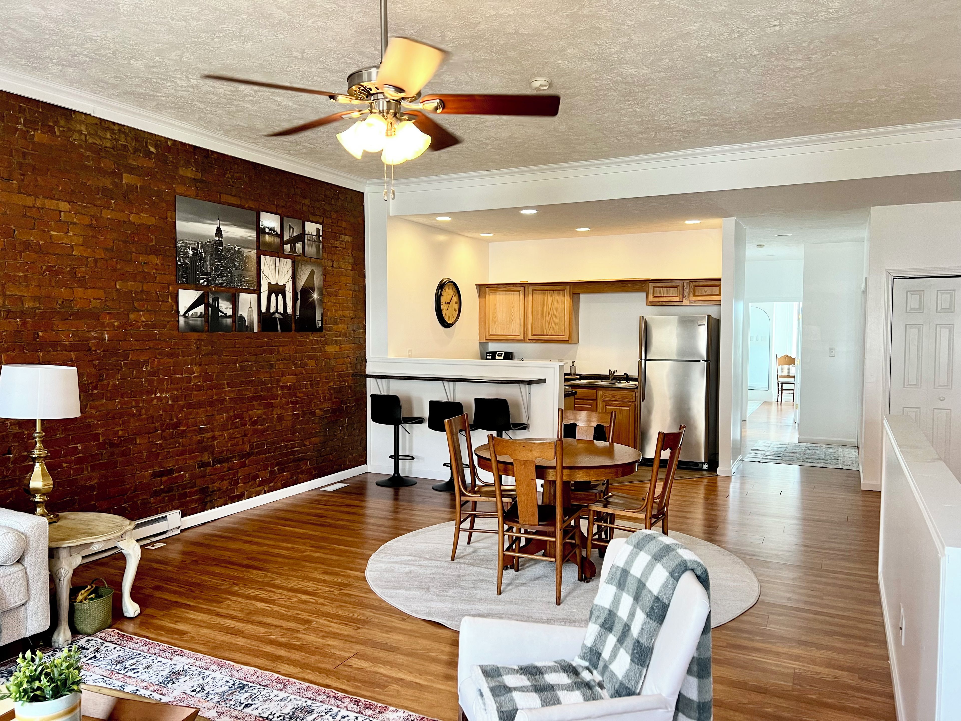 A spacious living area with a dining table, chairs, a ceiling fan, and a kitchen in the background.