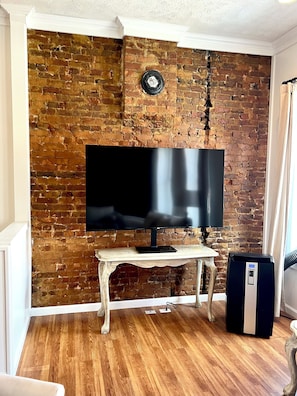 A room with a brick wall, a flat-screen TV on a wooden stand, and a black portable heater.