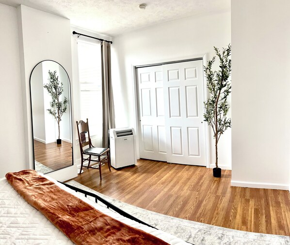 A room with a bed, a chair, a heater, a door, and a potted plant.