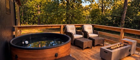 A wooden deck with a hot tub, outdoor furniture, and a fire pit.