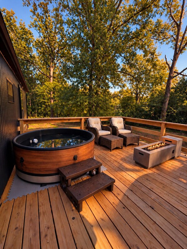 A wooden deck with a hot tub, outdoor furniture, and a fire pit.
