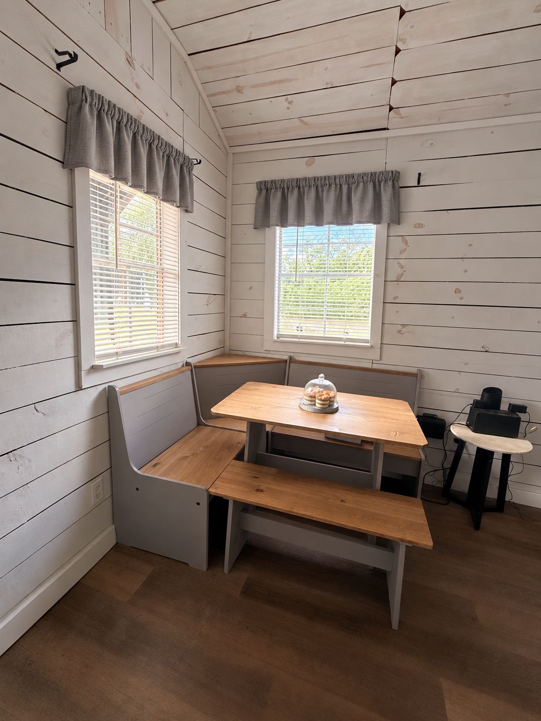 A corner room with a wooden bench, a table, and a window with blinds.